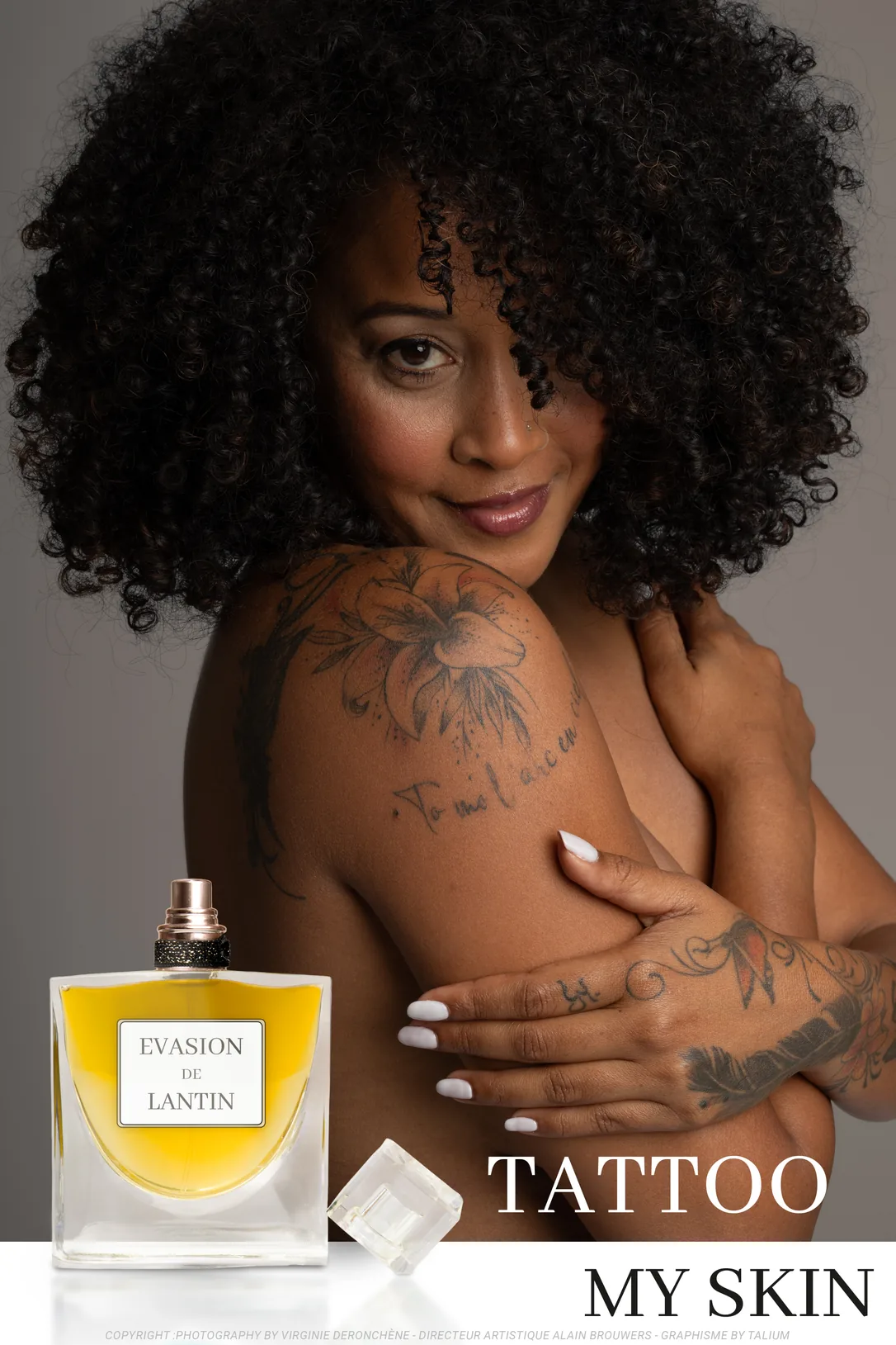 Affiche : une femme aux cheveux bouclés, l'épaule et le bras couverts de tatouages, serre son épaule dans ses bras et sourit à l'objectif. Un flacon de parfum jaune est posé en bas à gauche. Titre : Tattoo my skin.