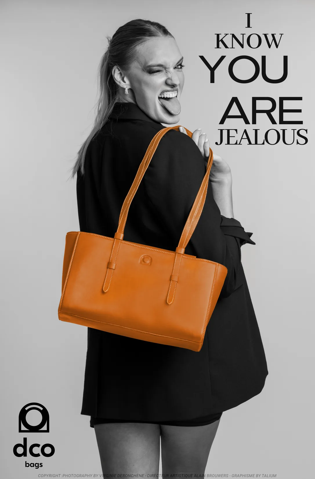 Affiche : en noir et blanc, une jeune femme en blazer noir tire la langue et cligne de l'œil par-dessus son épaule, un sac orange à l'épaule. Titre : I know you are jealous.