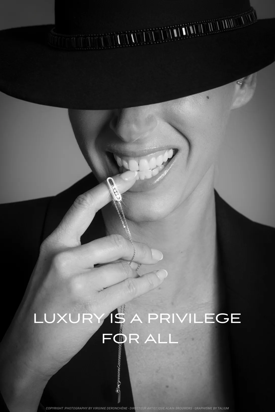 Affiche : en noir et blanc, le visage caché sous un chapeau noir, une femme sourit en mordillant du bout du doigt un pendentif en diamants. Titre : Luxury is a privilege for all.